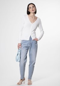 Cárdigan blanco de manga larga con cuello en V, cierre de botones y puños acanalados, combinado con jeans de tiro alto en azul claro y tacones con tiras.