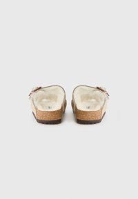 Kloskjorte med mykt beige overdel, faux fur foring og korktekstur såle, med en liten dekorativ sløyfe på siden.