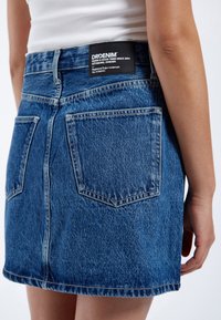 Gonna di jeans blu con vita aderente, tasche posteriori e orlo grezzo. Presenta un'etichetta nera con i dettagli del marchio sulla cintura.
