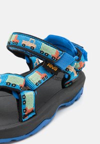 Mėlynos sandalai su raštuotais audinio diržais su sunkvežimių dizainu, juodu padu ir mėlynu apavu. Velcro diržai, leidžiantys reguliuoti dydį.