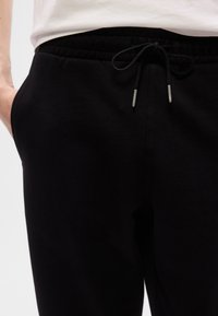 Μαύρο βαμβακερό τζόγκερ με ελαστική μέση και ρυθμιζόμενο κορδόνι. Διαθέτει πλαϊνές τσέπες και μαλακό, ελαστικό ύφασμα.