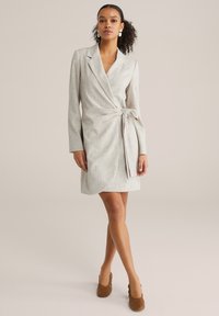 Vestito avvolgente grigio chiaro con maniche lunghe, vita annodata e tessuto strutturato. Presenta una profonda scollatura a V e un orlo all'altezza del ginocchio.