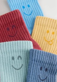 Värvikad soonikkoes sokid sinises, punases, kollases ja rohelises toonis, igaühel rõõmsameelne naeratava näo kujundus. Pehme, tekstuuriga kangas mängulise välimusega.