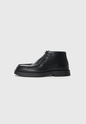 Botas de tobillo de cuero negro con puntera redondeada, suela de goma plana y dos cordones en la parte frontal. Textura suave con un detalle mínimo.