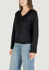 Maglione nero a collo a V con texture a costine all'orlo e alle maniche, caratterizzato da un corpo aderente e una vestibilità rilassata. Indossato con jeans azzurri chiari.