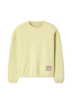 Sweat-shirt jaune clair à col rond, manches longues, avec un petit patch rectangulaire représentant des palmiers et un texte près de l'ourlet inférieur.