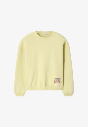 Lichtgele crewneck sweat met lange mouwen en een kleine rechthoekige patch met palm bomen en tekst dicht bij de onderzoom.