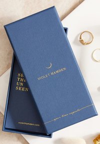 Indigo gemarmerde gift box met vergulde opdruk "Violet Hamden" en "jouw tijdcapsule," gedeeltelijk geopend om de binnenbekleding te onthullen.