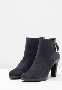 Stivaletti alla caviglia in suede blu navy con tacco alto, caratterizzati da un accento in pelle nera e un dettaglio con fibbia dorata sul lato.