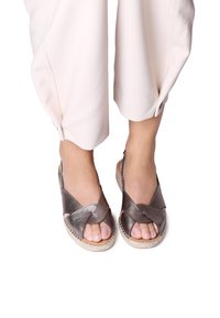 Metalliska bronsandaler med korsade remmar, öppen tå och vävda espadrillstil-sulor. Slät textur, lättvikt design.