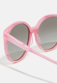 Ροζ μαρμάρινα γυαλιά ηλίου με γκρίζους φιμέ φακούς, κυκλικό σχήμα και λεπτά μπράτσα που φέρουν το όνομα της μάρκας "vogue" ανάγλυφο στο πλάι.