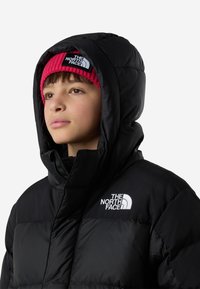 Geacă matlasată neagră cu glugă, având un logo alb pe piept. Sub glugă este purtată o cagulă roz cu dungi.