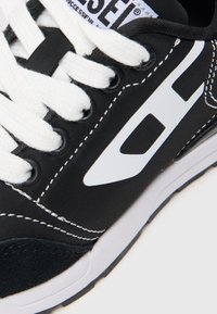 Fekete sneaker fehér fűzővel és varrással. Textíl felsőrész, hálós díszítések és fehér logó az oldalon. Gumitalp.