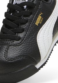 Čierne kožené tenisky so bielym pruhom a zlatým logom "Puma Roma". Majú textúrovaný povrch, čierne šnúrky a gumovú podrážku.