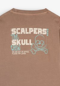 Bruine T-shirt met korte mouwen featuring witte versleten "SCALPERS" tekst, een doodskop en gekruiste botten afbeelding, en de zin "WE ZIJN NIET OP KANTOOR."