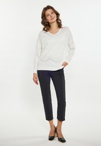 Witte v-hals gebreide trui met horizontale strepen en opengewerkte details, gecombineerd met zwarte cropped broek en zwarte hoge hakken.