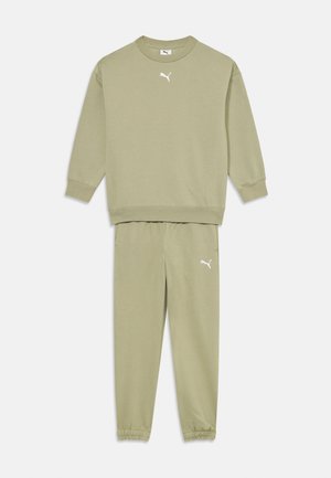 Olīvu zaļš džemperis un bikses, kas izgatavotas no mīkstas auduma. Iezīmē ribotas aproces, elastīgu jostu un baltas Puma logo akcents.