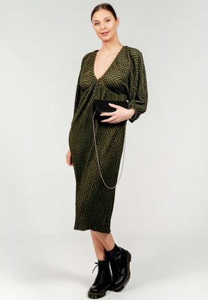 Abito midi verde a fantasia con scollatura a V profonda e maniche voluminose, abbinato a una borsa nera a pochette e stivali neri chunky.
