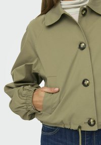 Khaki skrajšana jakna s ovratnikom, sprednjim gumbom, elastičnimi manšetami in stranskimi žepi. Zasnovana z vrvico na dnu.