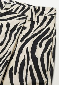 Gros plan sur un pantalon à rayures zébrées noires et blanches avec une taille boutonnée, des passants pour ceinture, une poche latérale et un détail plissé à l'avant.