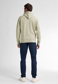 Sudadera color caqui con un corte relajado y capucha ajustable con cordones, combinada con jeans azul oscuro y zapatillas blancas. Textura suave, con un diseño minimalista.
