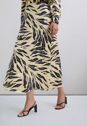 Larga falda beige con un patrón de rayas de tigre negro. La tela parece suave con una silueta fluida, combinada con tacones negros de tiras.