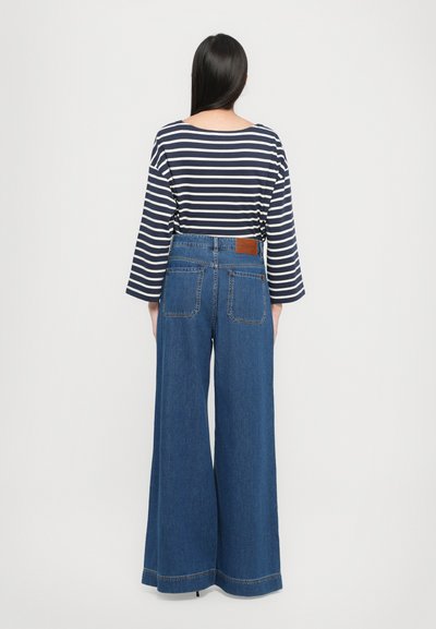 Maglietta a righe navy e bianca a maniche lunghe abbinata a jeans in denim blu a vita alta e gamba larga, con tasche posteriori e una toppa in pelle marrone.