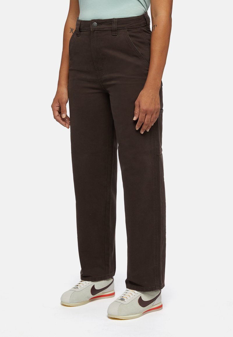 Bruine rechte broek gemaakt van stevig materiaal met zichtbare stikdetails, gecombineerd met lichtgrijze sportschoenen met een donker logo.