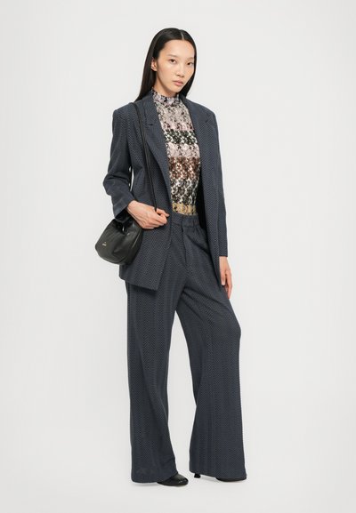 Abito in spina di pesce blu navy con una vestibilità rilassata, abbinato a un top con motivo multicolore e una piccola borsa nera.