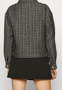 Svart och vit tweedjacka med en skarp krage, strukturerad väv och knäppte manschetter, tillsammans med en svart minikjol.