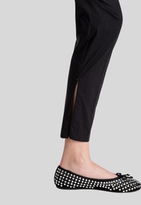 Pantaloni neri cropped con cerniere laterali, abbinati a ballerine nere decorate con strass trasparenti e un dettaglio a fiocco davanti.
