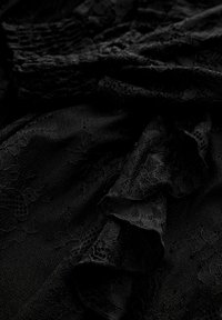 Tissu en dentelle noire présentant des motifs floraux élaborés et des volants texturés, superposés pour plus de profondeur et d'intérêt visuel. Texture douce et semi-transparente.