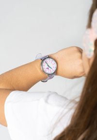 Montre analogique avec un bracelet en plastique transparent, un cadran rose, des index horaires blancs et des accents colorés. Décorée de cœurs et de points.