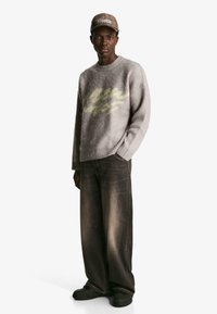 Szary, puszysty sweter z żółtym napisem, w połączeniu z luźnymi, ciemnymi dżinsami. Czarna para butów i brązowa czapka w wzory, noszone luźno.