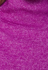 Pull à col roulé ajusté de couleur magenta vif avec un design côtelé texturé. Le matériau semble doux avec une légère variation de couleur sur toute la surface.