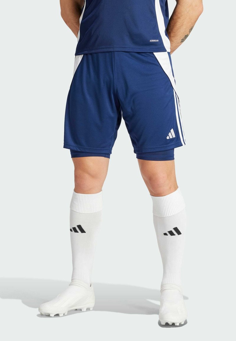 Shorts de sport bleu foncé avec des accents blancs, associés à des chaussettes blanches jusqu'aux genoux avec des rayures noires. Les shorts ont une texture lisse.