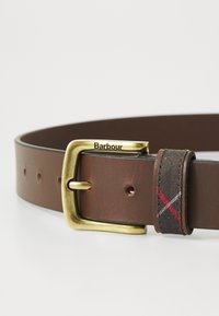 Brown leather belt with a brass buckle, featuring a patterned fabric loop with red and white accents. Multiple holes for adjustment.
