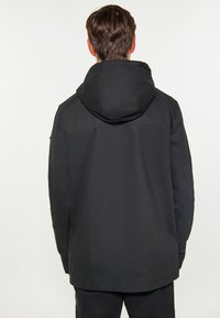 Chaqueta negra con capucha de diseño minimalista, con una textura suave y un corte ligeramente más largo, costuras visibles a lo largo de las uniones.