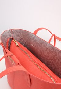 Czerwona skórzana torebka z teksturowanym zewnętrzem i gładką podszewką. Posiada złoty zamek błyskawiczny oraz dwa uchwyty do noszenia.