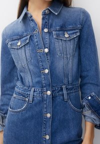 Jeansklänning i medelblå tvätt med långa ärmar, knapplist fram, två bröstfickor och knyt i midjan, med lätt blekningsdetaljer.