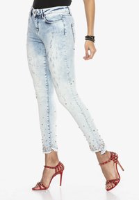 Jasnoniebieskie, zniszczone dżinsowe rurki z ozdobnymi brzegami. Noszone z czerwonymi sandałami na wysokich obcasach z ćwiekowymi akcentami.