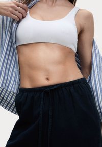 Biały prążkowany top typu crop top zestawiony z ciemnymi spodniami na elastycznym pasku, częściowo zakryty niebieską i białą w paski koszulą.
