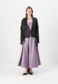 Jaqueta de motoqueiro de couro preto sobre um vestido de seda lavanda, com um corpete ajustado e saia fluida. Saltos altos pretos completam o visual.