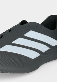 Baskets noires sans lacets avec surface texturée et trois grandes bandes blanches sur le côté, vue en angle montrant la tige et le talon.