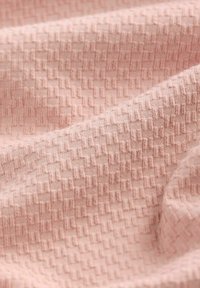 Struktureret stof i blød pink med et vævet mønster, der har små geometriske figurer. Overfladen fremstår let hævet med en glat finish.