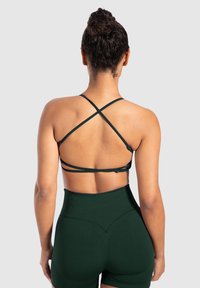 Sostén atlético de color verde oscuro con tirantes cruzados en la espalda y diseño ajustado, combinado con pantalones cortos de cintura alta, ambos con textura acanalada.