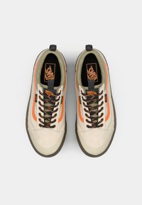 Zapatillas de lona beige con franja lateral naranja, cordones verde oscuro y suelas de goma. Cuenta con un acolchado en el tobillo y un logotipo en la lengüeta.