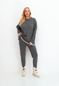 Suéter de punto gris con cuello redondo y remates blancos, combinado con pantalones jogger grises a juego y botas en color crema con detalles de hebilla.