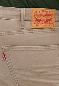 Les jeans Levi's 511 en beige présentent une étiquette rouge et un label de marque orange avec des graphismes distinctifs, une texture lisse et des éléments de design classiques.