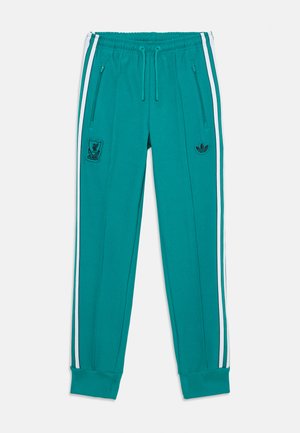 Joggers en color verde azulado, hechos de una tela suave, con franjas laterales blancas, bolsillos con cremallera y logotipos bordados en el muslo. Diseño de estilo atlético.